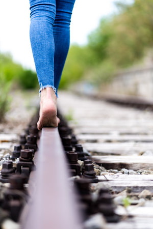 A vertical shot of a female in jeans walking through the train rails barefootの写真素材