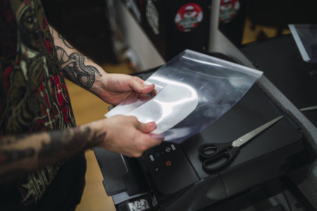A shot of a tattoo artist with tattoed arms  laminating a new tattoo in the laminating machineの写真素材