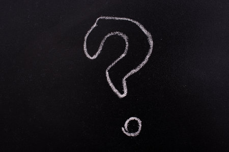 A closeup of a question mark written with a chalk on a blackboardの写真素材
