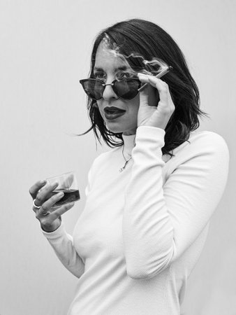 Stylish Woman Smoking a Joint Outside with Gray Background and glass of rose wine.  Black and White.