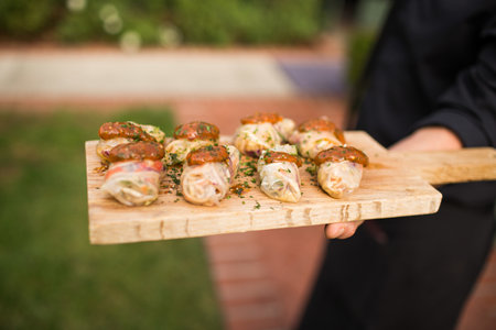 A closeup shot of a person holding a wooden board with shrimp rolls on it at a private eventの写真素材