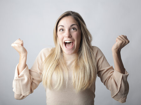 A young blonde woman with an open mouth showing the emotion of happiness behind a white background