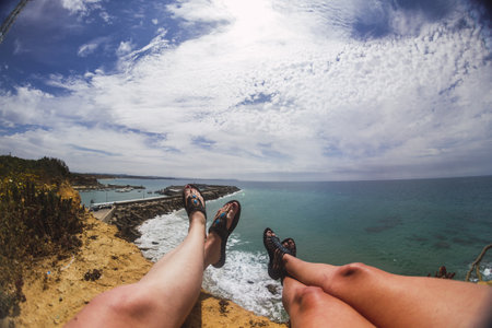A closeup shot of the legs of people lying on the rocks surrounded by the sea under the sunlightの写真素材