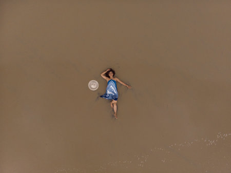 An aerial shot of an Asian female lying on a sandy beach