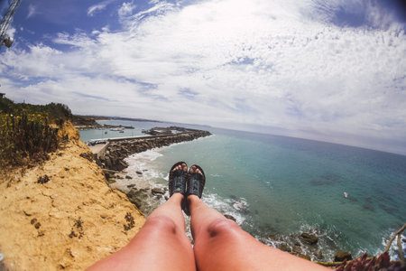 A closeup shot of the legs of a person lying on the rocks surrounded by the sea under the sunlightの写真素材