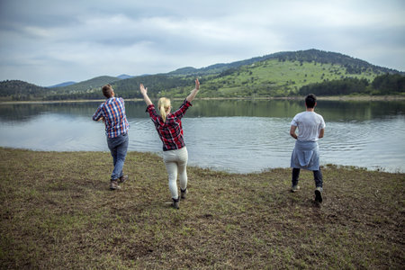A back view of young friends throwing stones into the waterの写真素材