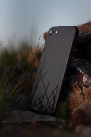 A vertical closeup shot of a black smartphone leaned on a  stone