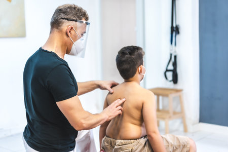 A physiotherapist wearing a face mask giving back massage to a young patientの写真素材