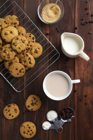 A high angle shot of Chocolate chip cookies, milk in a jug and coffee in a cup on a wooden table