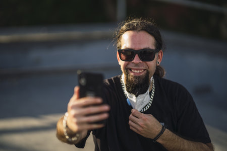 A selective focus shot of a smiling bearded male taking a selfie from his phone while removing his face maskの写真素材