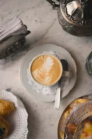 A vertical shot of a cup of cappuccino on the marble table with dessertsの写真素材