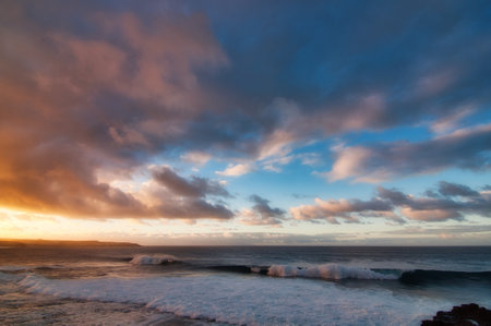 A breathtaking view of a calm sea under a cloudy sky at sunsetの写真素材