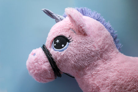 Childrens girly pink unicorn stuffed animal/ plush toy head, on a baby blue background. Black wire used as noseband/muted to keep quiet. Concept photoの写真素材