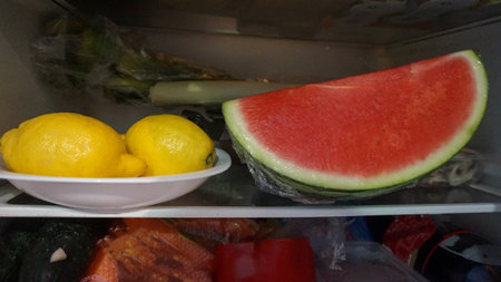 A closeup of lemons on a white plate and fresh watermelon slice in a fridgeの写真素材
