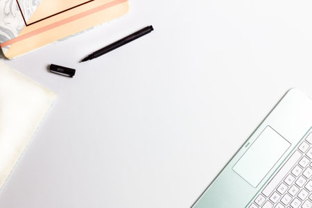 A high angle shot of a laptop keyboard and a notebook with a black pen on a white surface
