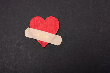A closeup shot of a red heart with a plaster isolated on a black backgroundの写真素材
