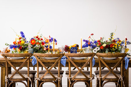 A horizontal shot of a table with wooden chairs decorated with colorful flowers and candlesの写真素材