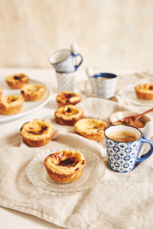 A vertical shot of delicious Portuguese egg tarts with a cup of espresso on a white tableの写真素材