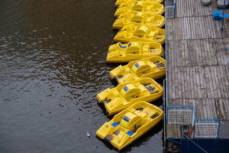 A high angle shot of the yellow pedal boats tired to the wooden pier on the calm surface of the waterの写真素材