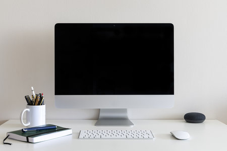 A work desk with a computer, a cup with pens and pencils against a white wallの写真素材