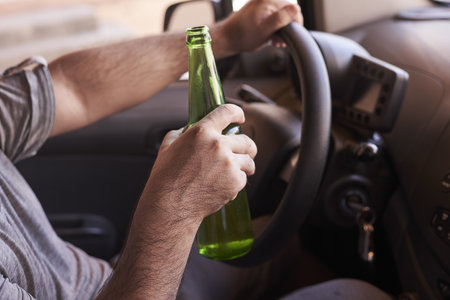 A bottle of beer in a man's hands driving the car during daytime