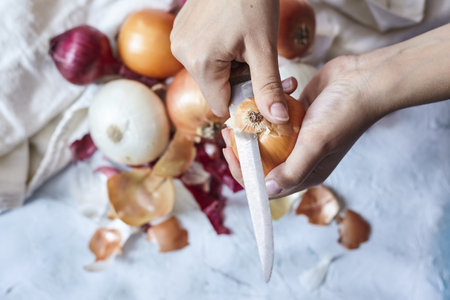 A person cutting the onion with a knife over other types of onionsの写真素材
