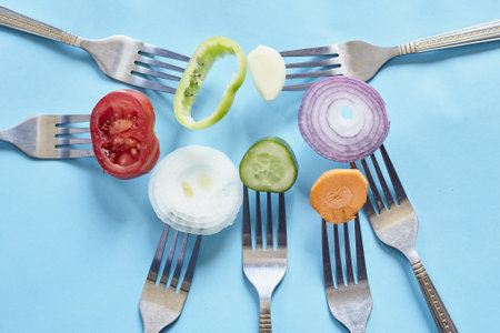 A top view of sliced pieces of fresh vegetables and spices on forks against a blue backgroundの写真素材