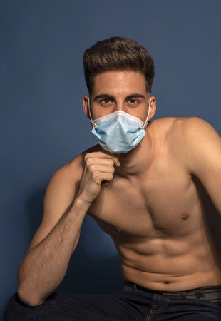 A shallow focus shot of a young male with a medical mask isolated on blue backgroundの写真素材