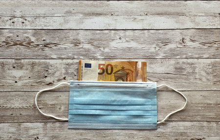 A protective mask and euro on wooden table- COVID-19の写真素材