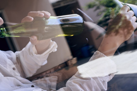 A woman driving a car while drinking beer from a bottle as seen through a car glass window. Drunk...