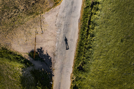 An aerial shot of a person standing in the middle of the road surrounded with greeneryの写真素材