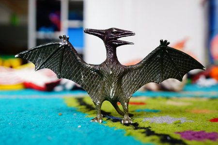 A closeup of a black toy dragon on a colorful carpet under the lights with a blurry backgroundの写真素材