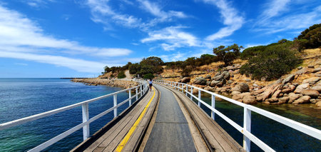 A panoramic shot of an empty road surrounded by the sea and hills