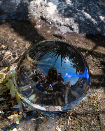 A vertical closeup shot of a crystal ball on the ground reflecting the rocks and the sky