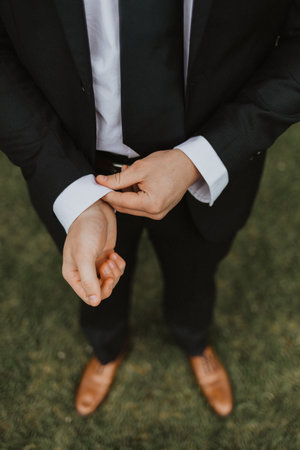 A high angle shot of the groom's hands fixing his cuffs while standing in a forest