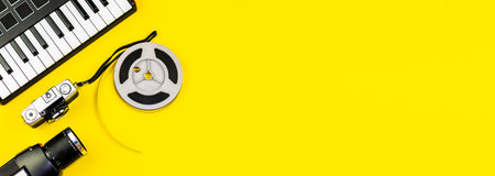 A top view of cameras, film reel and a piano keyboard on a yellow surface. Music video, vlog hobby conceptの写真素材