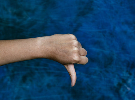 A horizontal shot of a hand showing thumbs down on a marbled blue backgroundの写真素材