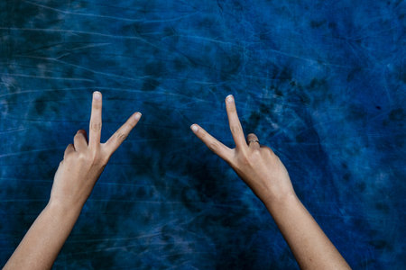 A horizontal shot of two hands showing a peace/victory sign on a blue marble background