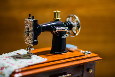 A selective focus shot of a small sewing machine with a blurred wooden background