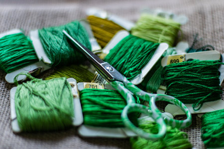 A closeup shot of colorful yarn rolls on a piece of fabric with cross-stitch art of purple grapesの写真素材