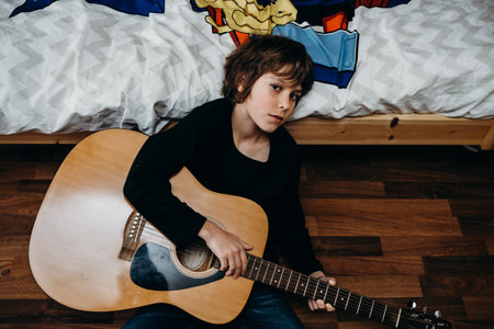A young fair-haired boy sitting on the floor and holding a guitar