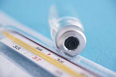 An extreme closeup of a vaccine vial and thermometer against a blue background. Vaccine, medicine, protection, COVID19, coronavirus conceptの写真素材