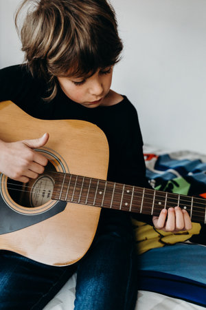 A vertical shot of a white young boy playing guitar in the bedroomの写真素材