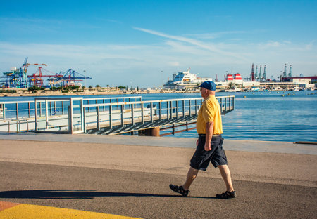 A horizontal bright view of a senior man walking in a city shore on a sunny dayの写真素材