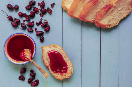 A high angle shot of fresh bread, homemade rosehip jam and dried rosehips on a wooden blue surfaceの写真素材