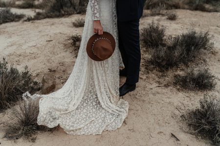 A bride holding a hat and a groom standing near the bushesの写真素材
