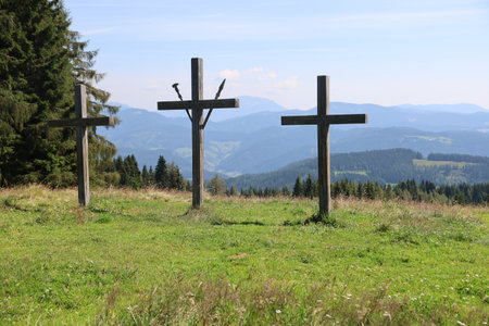 An eye-level shot of three wooden crosses on green mountains covered in lush forestsの写真素材