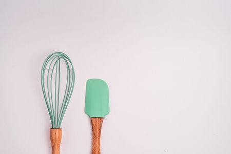 A closeup shot of green kitchen whisk and shovel isolated on a light-colored backgroundの写真素材