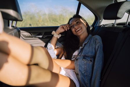 A horizontal shot of a beautiful young caucasian female posing in the back seat of a car in a fieldの写真素材