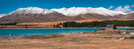 A panorama shot of Lake Tekapo in New Zealand surrounded with snowy mountainsの写真素材